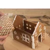 A person is assembling a gingerbread house, attaching a roof piece to the main structure. Voir les images du produit