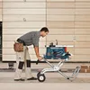 A man is using a Bosch table saw on a stand in a workshop. Voir les images du produit