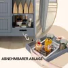 A hand is holding a tray with a cupcake, a bottle of juice, and two glasses, placed on a magazine. In the background, a gray kitchen cart is visible, filled with food items. Voir les images du produit