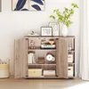 A wooden cabinet with two doors open, displaying shelves filled with books, decorative items, and storage boxes. The cabinet is placed in a room with a painting on the wall and a window with curtains. Produktbild-Vorschau
