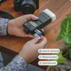 A person is inserting batteries into a camera flash unit on a wooden table. Produktbild-Vorschau
