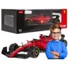 A red remote-controlled Ferrari Formula 1 car is shown in its packaging and also outside of the box, with a young boy standing next to it. Podgląd zdjęcia produktu