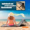 A woman in a bikini and hat sits on a beach mat on a sandy beach, facing the ocean. A beach chair is set up behind her. Produktbild-Vorschau