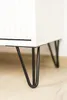 Close-up of black hairpin legs attached to a white furniture piece, resting on a light wooden floor. Podgląd zdjęcia produktu