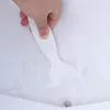 A hand is using a white plastic scraper to remove ice from a white surface, possibly a refrigerator or freezer. Produktbild-Vorschau