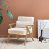 A fluffy white armchair with a wooden frame is placed in a room with a terracotta-colored wall and a patterned rug. Produktbild-Vorschau