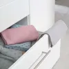 A close-up view of an open drawer in a white dresser, showing folded textiles inside and one draped over the edge. Produktbild-Vorschau