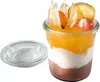 A layered dessert in a glass jar with fruit on top, next to its glass lid. Náhled obrázku produktu