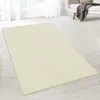 A cream-colored rug is laid out on a light wooden floor in a room with sheer white curtains in the background.
