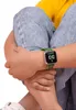 A child wearing jeans and a yellow shirt is sitting with their legs crossed, showing off a green Minecraft-themed watch on their wrist. Produktbild-Vorschau