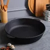 A black cast iron pan is placed on a gray countertop, with kitchen utensils and cutting boards in the background. Produktbild-Vorschau