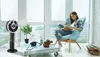 A woman is reading a book in a chair next to a fan and a table with a camera and plants. Produktbild-Vorschau
