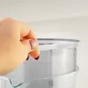 A hand is shown holding a clear plastic ring that is part of a water filter pitcher. Produktbild-Vorschau
