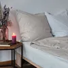 A bed with pillows and a duvet, a bedside table with a candle and books. Produktbild-Vorschau
