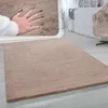 A hand is shown pressing into a soft, beige rug in a living room setting. Anteprima dell’immagine prodotto