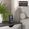 A CO2 measuring device is placed on a nightstand next to a potted plant and a bed. Produktbild-Vorschau