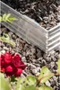 A close-up view of a metal garden bed border with rocks and a red rose in the foreground. Produktbild-Vorschau