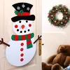 A festive snowman decoration hangs on a door next to a Christmas wreath and a teddy bear. Náhľad obrázku produktu
