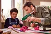 A father and son are crafting together at a table, using a hot glue gun to assemble paper flowers. Produktbild-Vorschau
