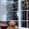 A teddy bear sits in front of a window decorated with string lights and a Christmas wreath. Produktbild-Vorschau