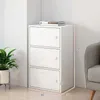 A white three-drawer cabinet is shown in a corner of a room, next to a plant and a chair. Dimensions are indicated with numbers. Produktbild-Vorschau