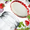 A close-up shot of a glass jar and its lid, surrounded by floating ingredients like tomatoes, cucumber, and red onion. Podgląd zdjęcia produktu