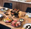 A raclette grill set up on a dining table with various food items, ready for a meal. Produktbild-Vorschau