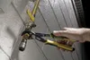 A person's hand is using a pair of pliers to adjust a brass pipe fitting attached to a wall. Voir les images du produit