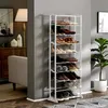 A white shoe rack filled with shoes, placed next to a wall and a floor lamp. There is also a cabinet and a chair visible. Produktbild-Vorschau