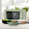 A retro-style green microwave is displayed on a table with three bowls of food in front of it. Produktbild-Vorschau