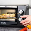 A person's hand is shown adjusting the timer on a toaster oven, which is baking a pizza. Voir les images du produit