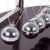 A close-up of a Newtons Cradle with several silver balls hanging from strings. Náhľad obrázku produktu