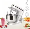 A white and silver stand mixer with various attachments, a smoothie, and fruit on a white surface. Produktbild-Vorschau