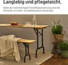 A wooden table and bench set with a blanket draped over the bench, set up on a patio with plants. Produktbild-Vorschau
