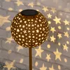 A solar-powered decorative garden light shaped like a sphere with star cutouts, casting star-shaped light patterns on a brick wall. Produktbild-Vorschau