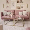 A pink couch with decorative pillows and a bouquet of flowers sits in a living room setting, with two gold and glass coffee tables in front of it. Produktbild-Vorschau