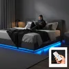 A woman is reading a book on a bed with blue LED lights. Produktbild-Vorschau