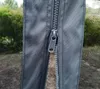 Close-up of a zipper on a gray fabric, with a mesh screen visible to the left and trees in the background. Voir les images du produit