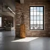 An interior shot of a loft-style apartment with exposed brick walls, concrete floors, and large windows overlooking a city skyline. A wooden pedestal with a metallic sculpture is placed in the foreground. Anteprima dell’immagine prodotto