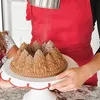 A person is dusting powdered sugar onto a pine forest-shaped Bundt cake. Anteprima dell’immagine prodotto