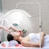 A woman is lying on a massage table while a person performs a facial treatment under a ring light. Produktbild-Vorschau