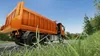 A dump truck is driving on a road next to a grassy area and trees. Produktbild-Vorschau