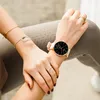 A woman's hands wearing jewelry and a smartwatch, resting on her legs. Produktbild-Vorschau