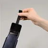 A hand is holding a dark blue pouch with a smartphone inside, pulling it out by a black strap. Produktbild-Vorschau