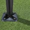 A close-up view of a dark gray metal base plate with a black pole attached, secured by four bolts, resting on artificial green grass. Náhľad obrázku produktu