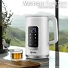 A white electric kettle with a digital display is shown on a countertop, with a glass of tea next to it. The background features a scenic view of mountains and trees through a window. Náhled obrázku produktu