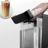A hand is adding ice to an ice maker, with a glass of iced coffee in the background. Produktbild-Vorschau