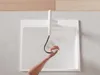 A person's hand is holding a faucet spray head over a white sink, with water spraying into the sink. Produktbild-Vorschau
