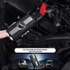 A person is holding a car battery jump starter device next to a car engine. Produktbild-Vorschau