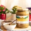 A jar of honey with propolis, two bowls of honey, and potted plants in the background. Produktbild-Vorschau